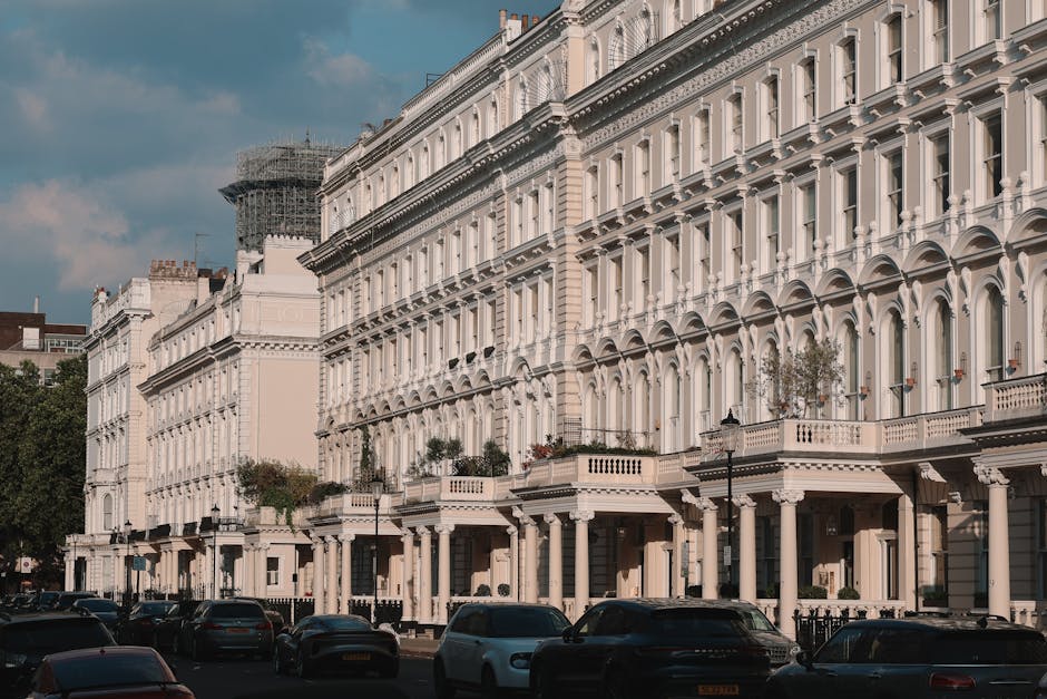 A row of elegant Victorian-style terraced houses situated along Barnes High Street, with white facades featuring decorative mouldings, large sash windows, and small front gardens with potted plants. S