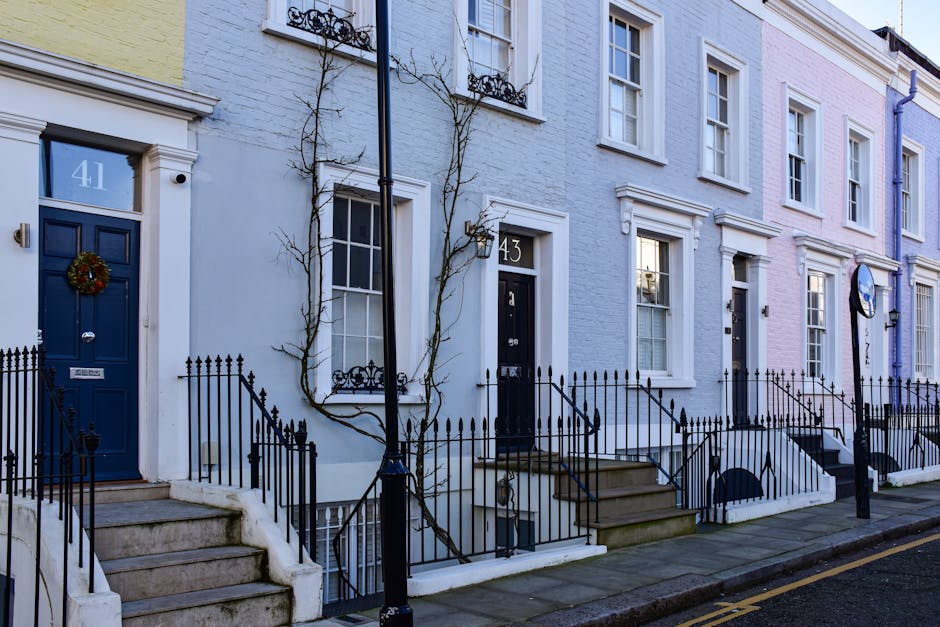 A row of elegant Victorian-style terraced houses situated along Barnes High Street, with white facades featuring decorative mouldings, large sash windows, and small front gardens with potted plants. S